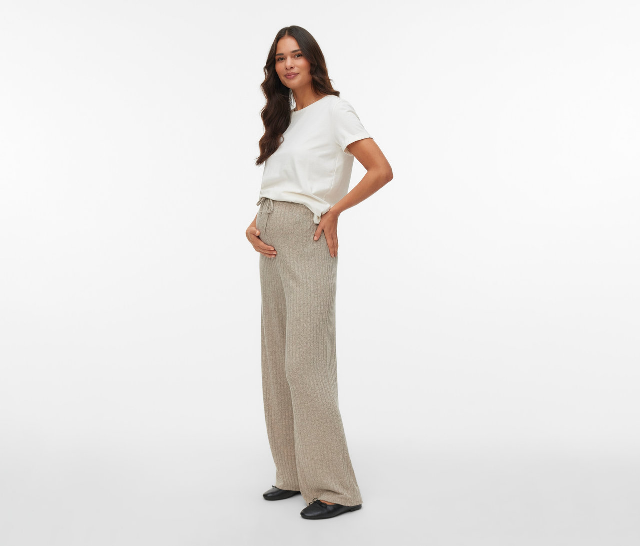 Tehotná žena pózuje v nohaviciach MAMALICIOUS Loosefit »MLPAMMIE« a bielom tričku, s rukou na bruchu.