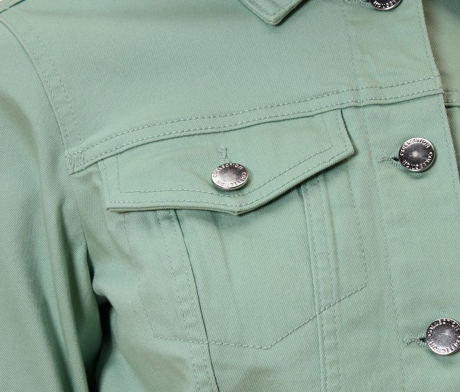 Detail záberu svetlozelenej bundy so striebornými gombíkmi a náprsným vreckom.