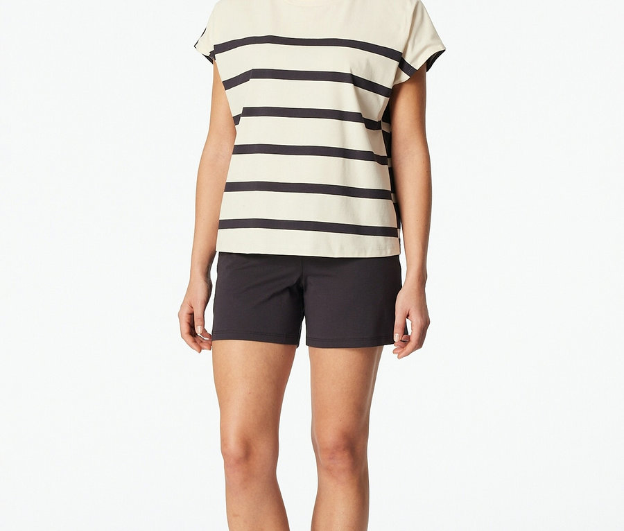 Žena stojí naboso na bielom pozadí v pruhovanom tope a čiernych šortkách.