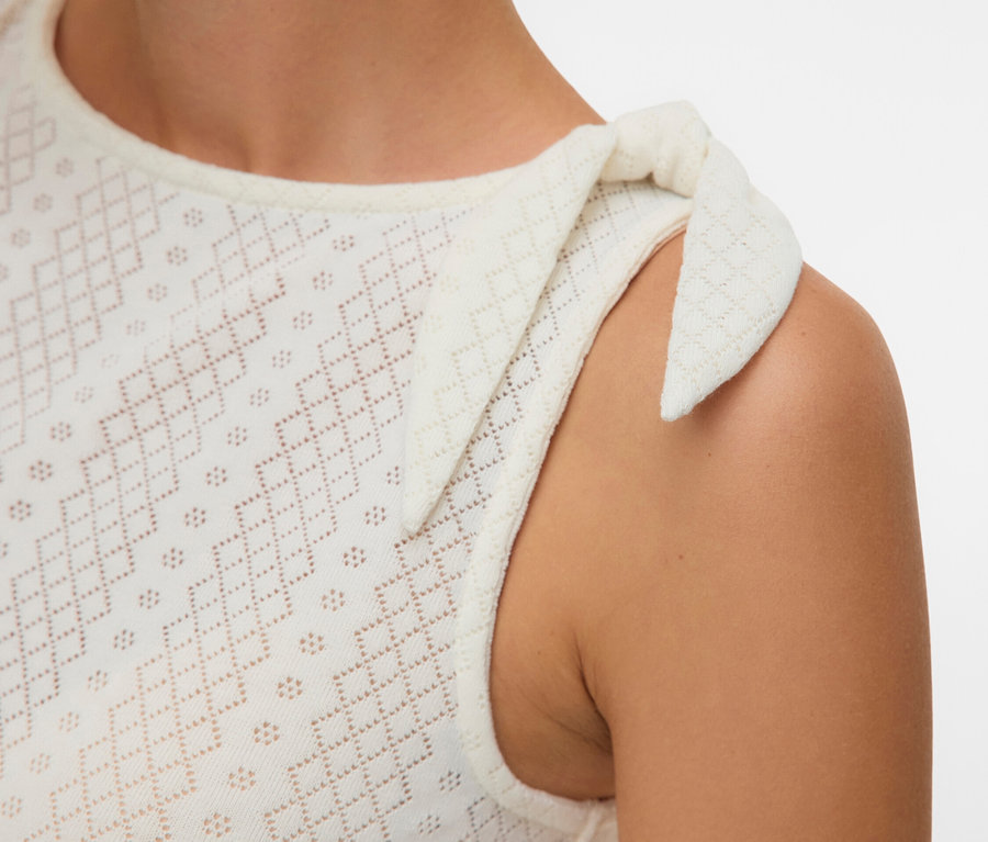 Detail ženy v bielom dierkovanom tielku s mašľou na ramene.