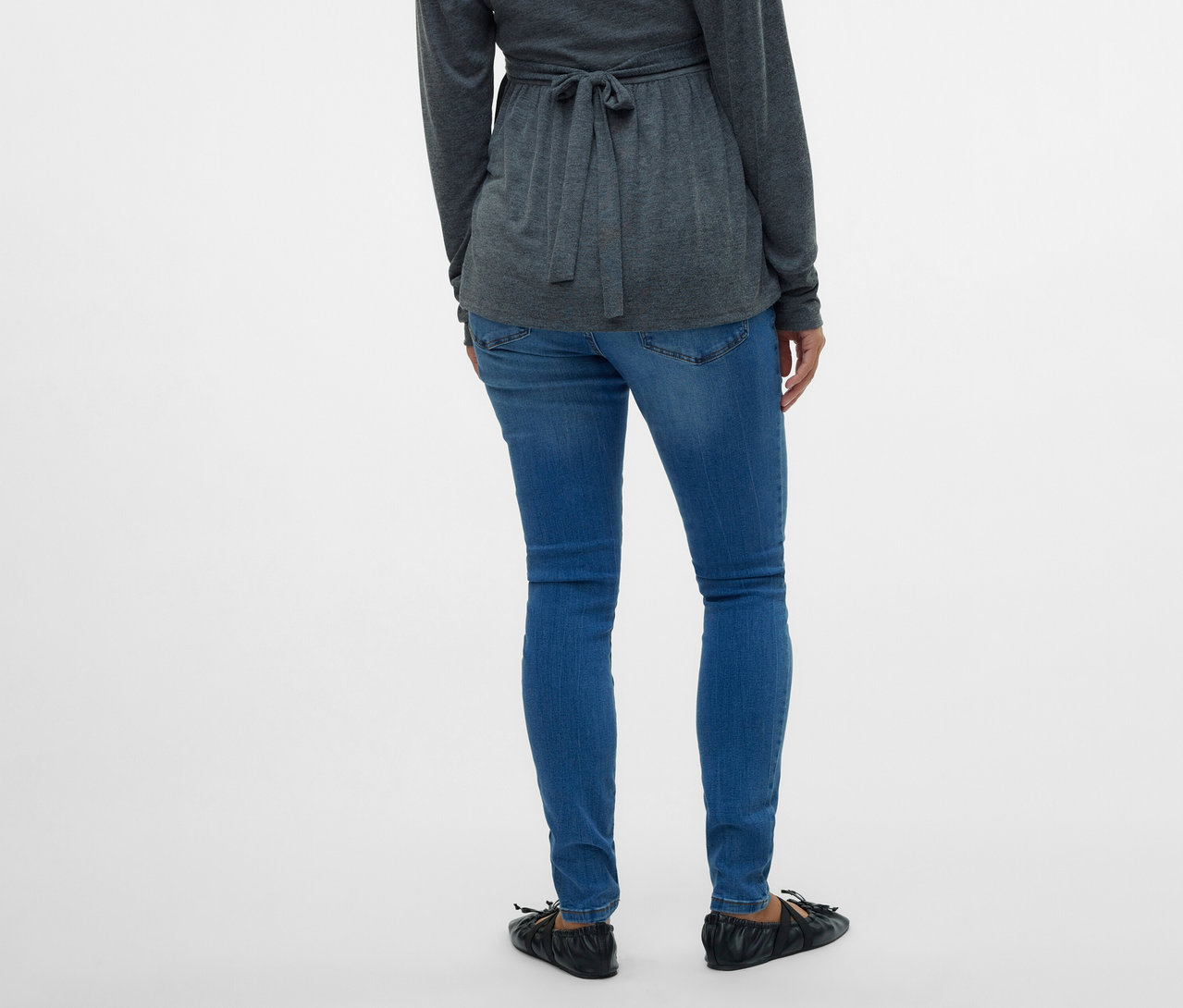 Pohľad zozadu na ženu v šedej blúzke so zaväzovaním a skinny džínsoch MAMALICIOUS »MLMILA« na bielom pozadí.