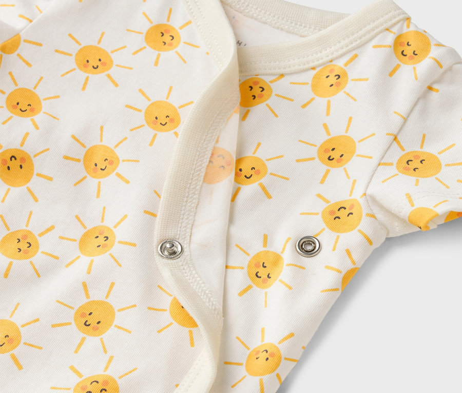 Detail bielych detských body s potlačou žltých slniečok a patentkami.