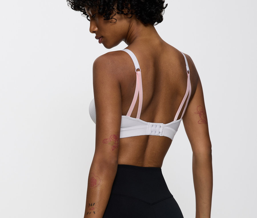 Žena má na sebe bielu športovú podprsenku s ružovými ramienkami a čierne legíny.