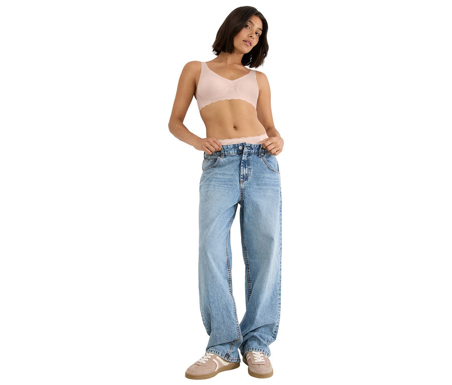 Žena s krátkymi hnedými vlasmi v svetloružovej čipkovanej podprsenke, širokých svetlomodrých džínsoch a svetlohnedých teniskách.