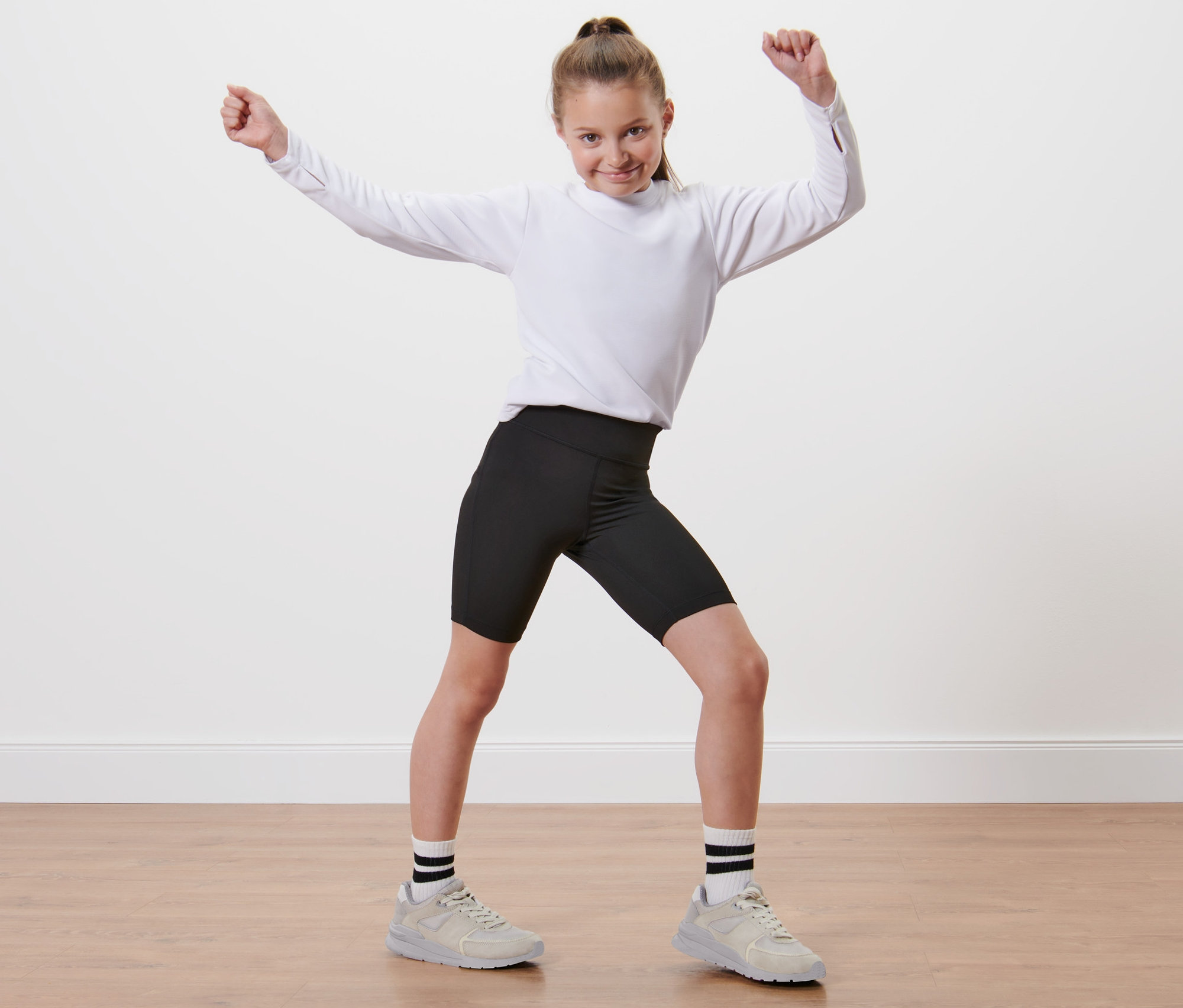 Dievča v bielom tričku a detských cyklistických šortkách, 2 ks stojí s rukami hore.