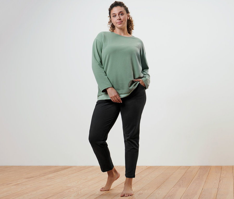 Žena pózuje v oversized fitness tričku s dlhými rukávmi a čiernych teplákoch.