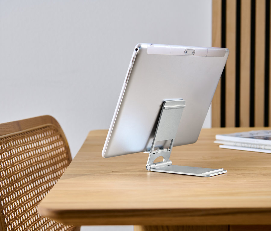 Tablet je opretý o stojan na smartfón a tablet na drevenom stole.