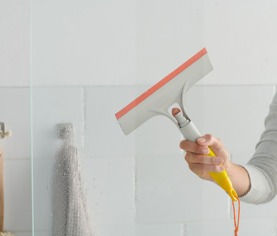 Žena používa stierku na okná 3 v 1 na sklenené sprchové dvere.