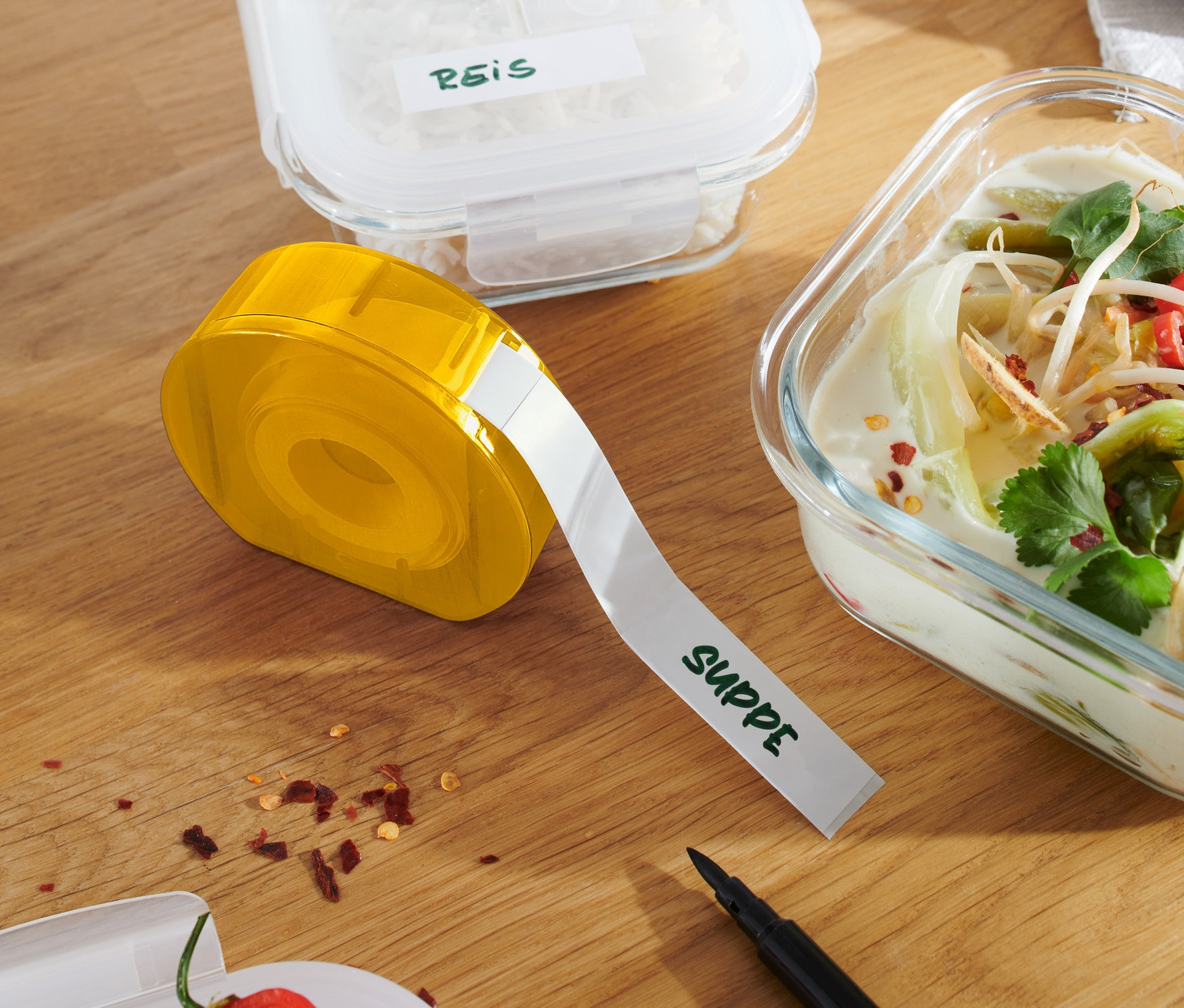 Žltý zásobník na etikety na drevenom stole vedľa nádob s ryžou a polievkou.