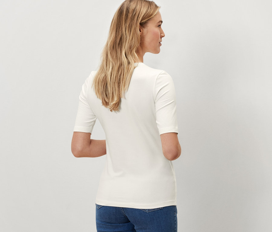 Pohľad zozadu na ženu v krémovom tričku s polodlhým rukávom a modrých džínsoch.