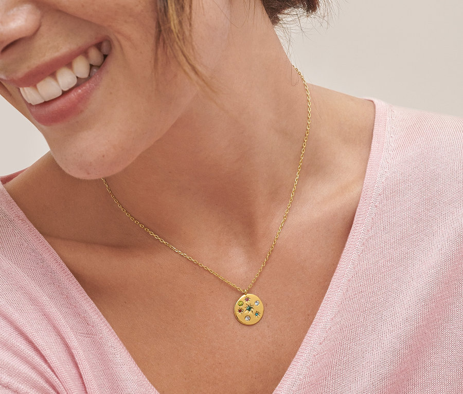 Detail usmievajúcej sa ženy s náhrdelníkom s okrúhlym viacfarebným príveskom a náušnicami kreoly s viacfarebným príveskom.