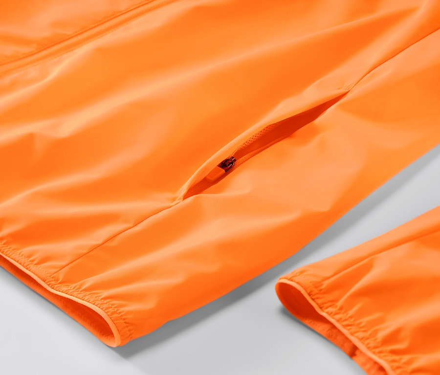 Detail neónovo-oranžovej vetruvzdornej bežeckej bundy so zipsom.