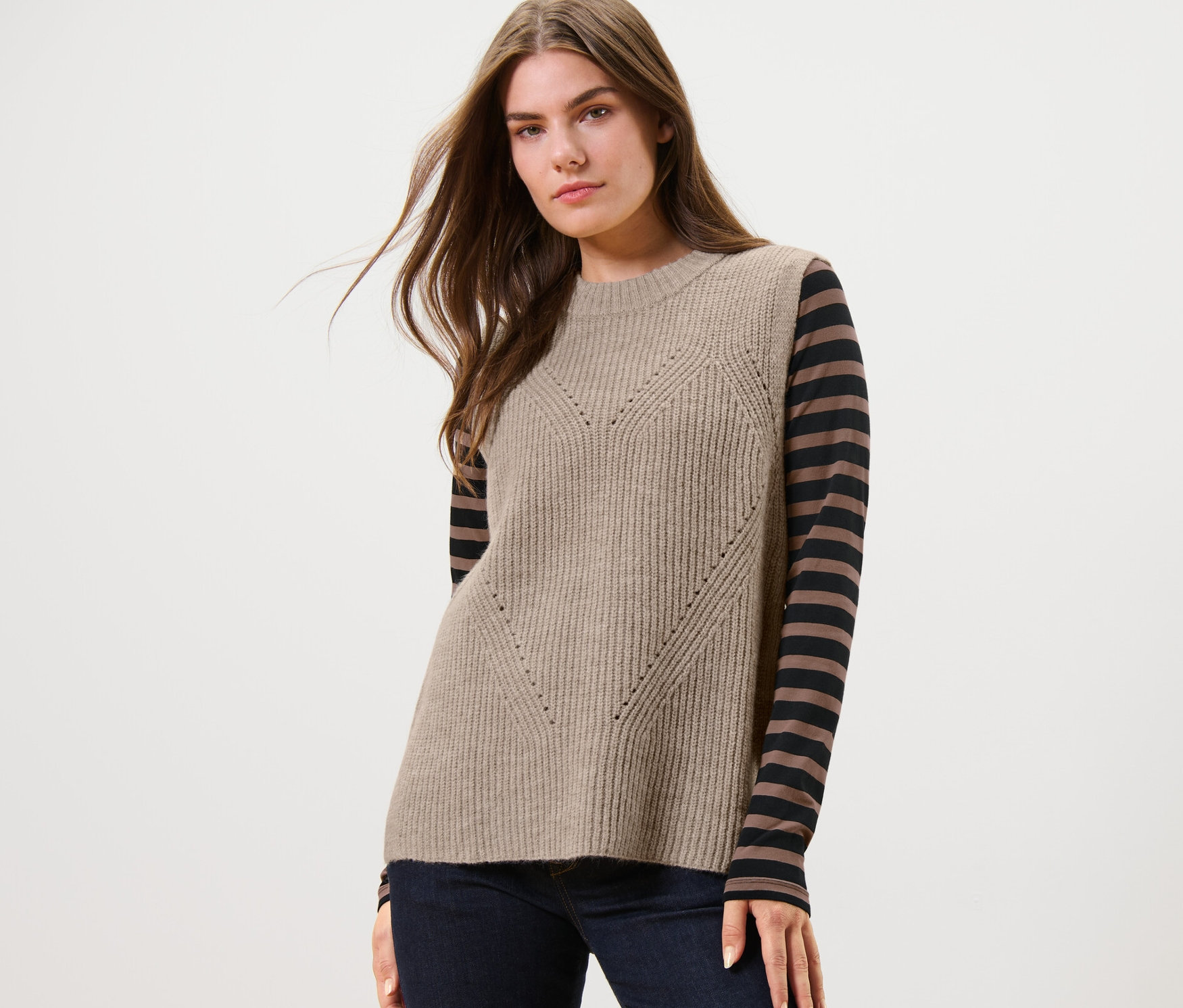 Žena má na sebe pletenú vestu béžovej farby s melírom.