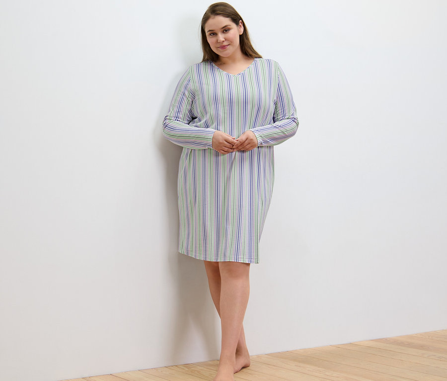 Žena v nočnej košeli s prúžkami stojí pri stene.