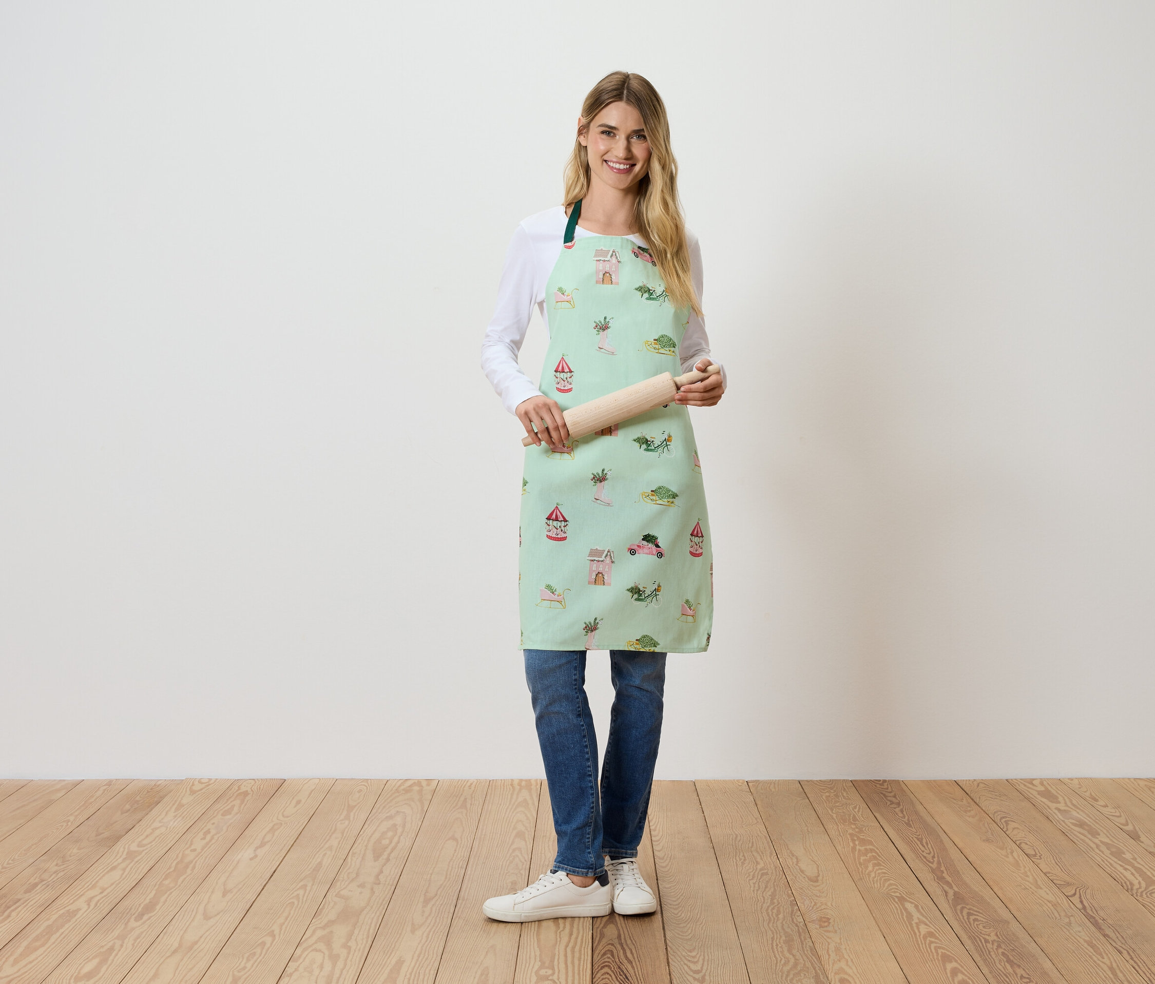 Žena stojí a drží valček na cesto. Má na sebe svetlozelenú zásteru s potlačou.