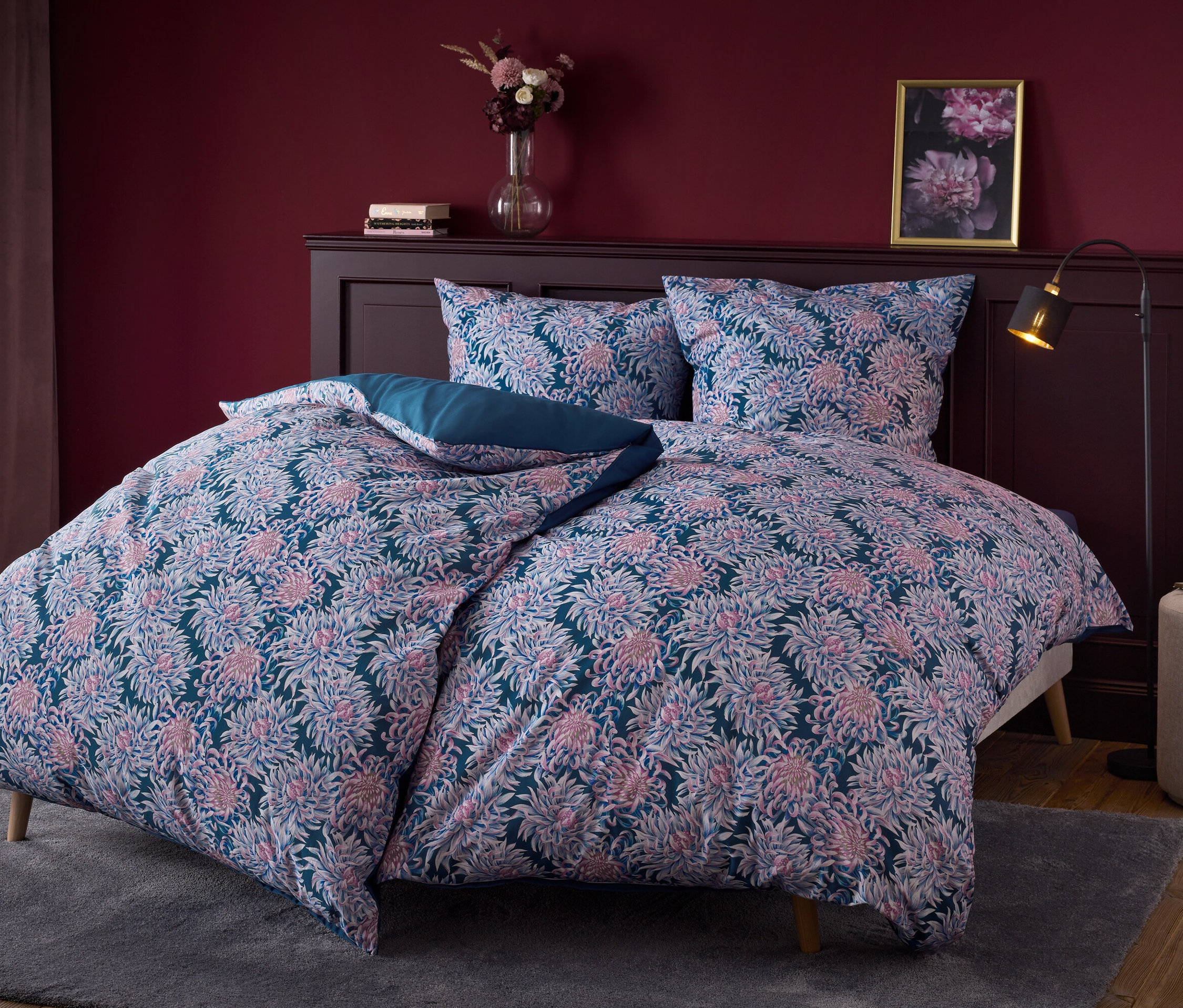 Kvetinové posteľné prádlo na posteli s čelom z tmavého dreva.