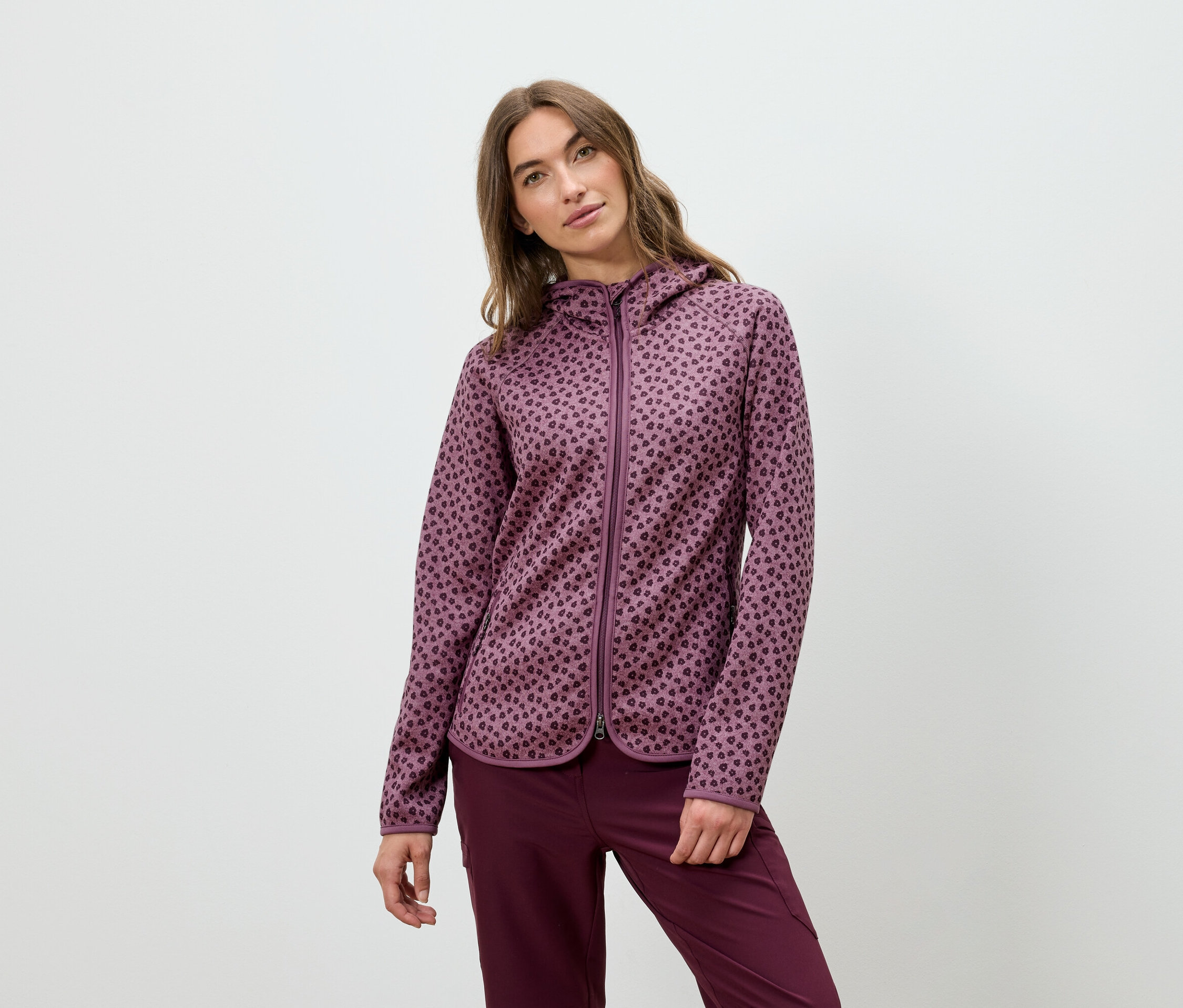 Žena pózuje v bordovej mikine s kapucňou a nohaviciach.