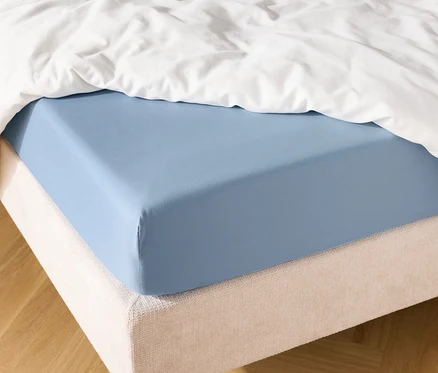 Svetlomodrá napínacia plachta na posteli s bielou prikrývkou.