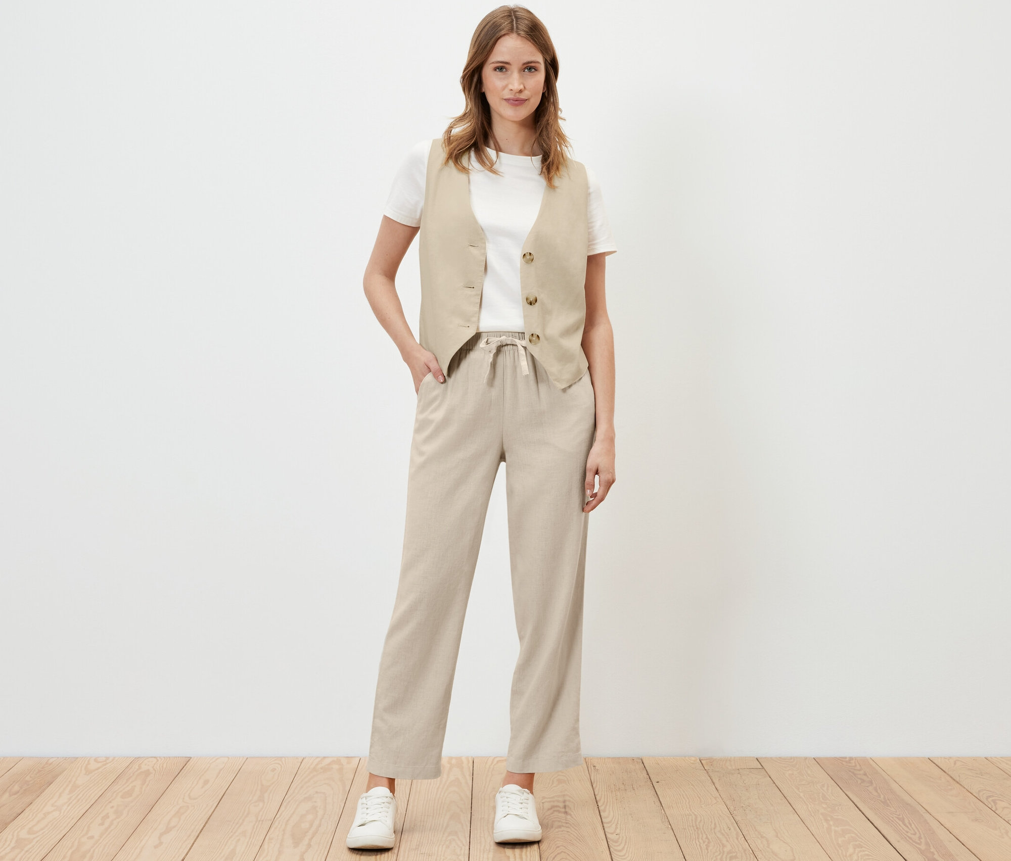 Žena pózuje v pieskových ľanových nohaviciach a veste.