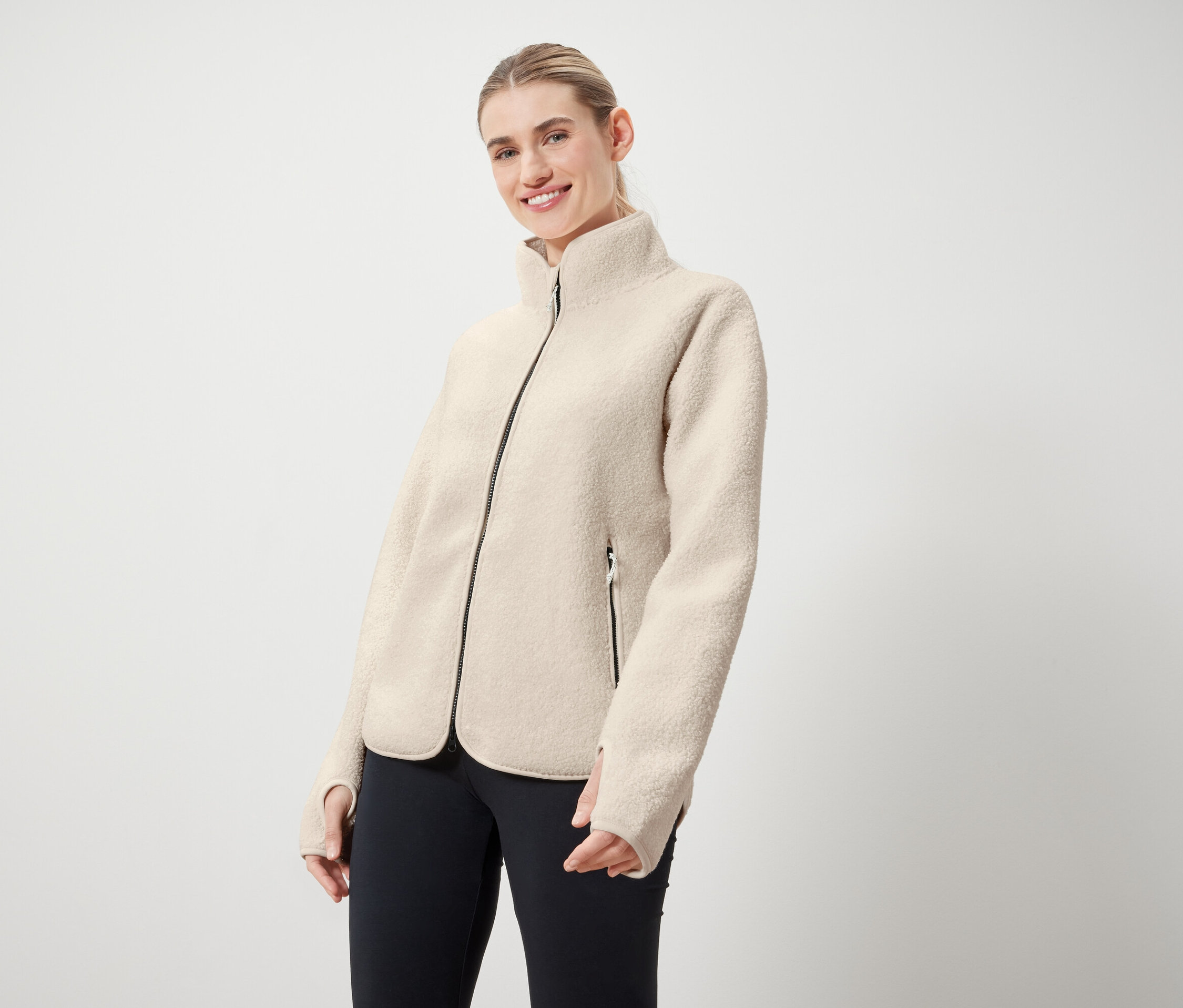 Žena má na sebe krémovú bundu s čiernym zipsom a čierne legíny.