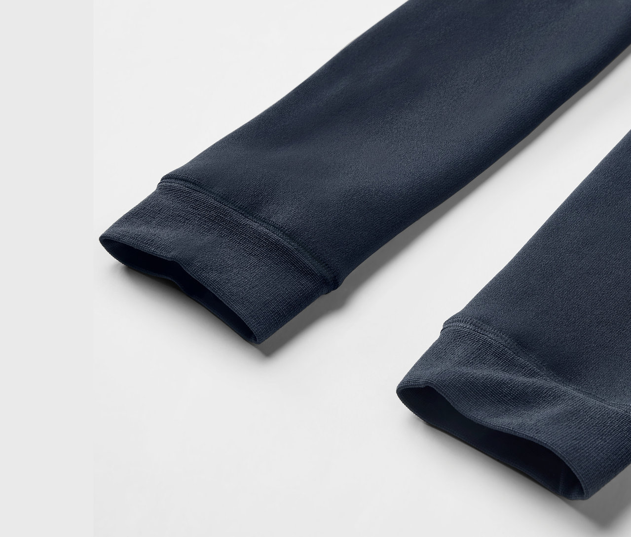 Detail dvoch rukávov tmavomodrej mikiny s rebrovanými manžetami na bielom pozadí.