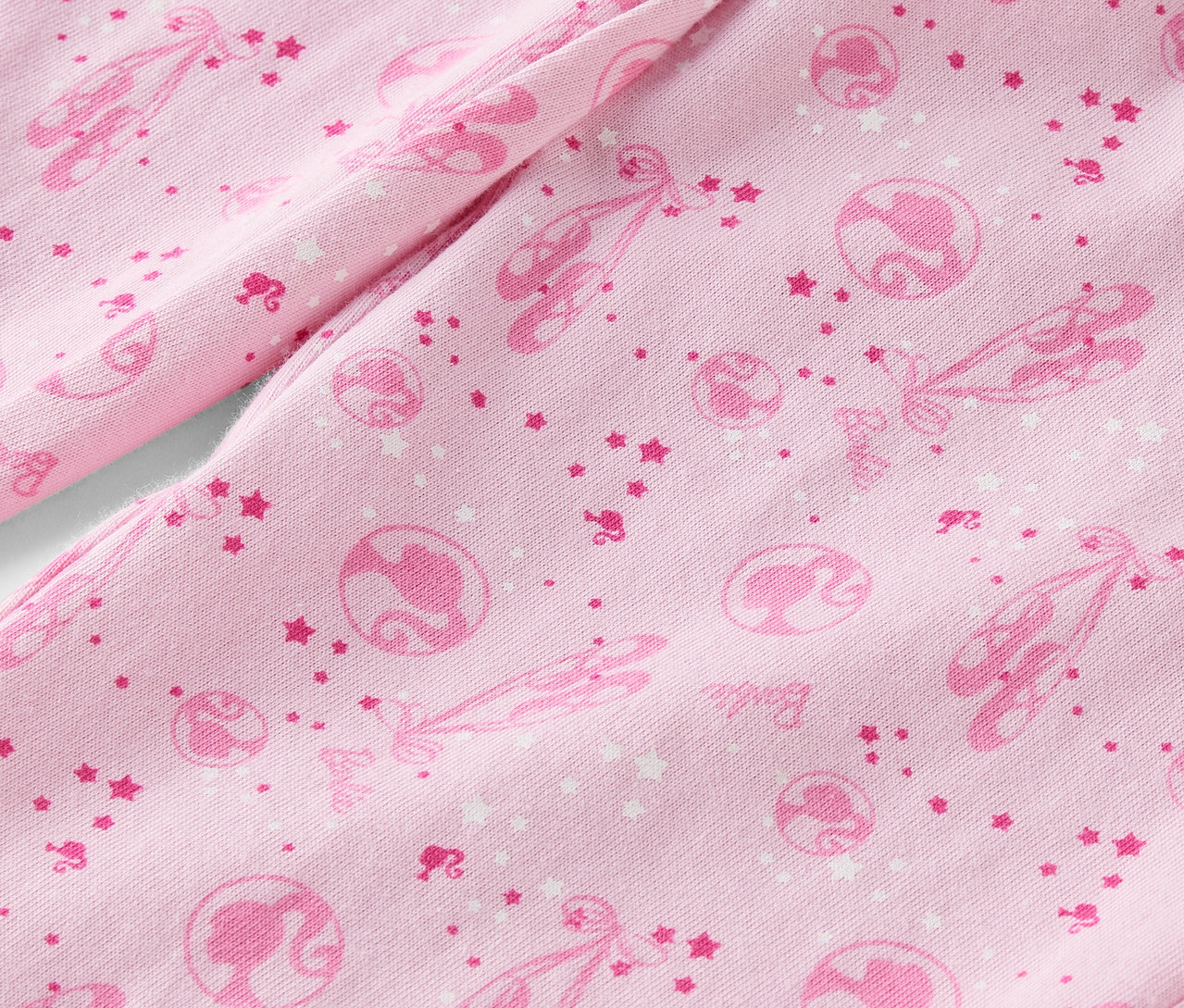 Detail ružovej látky s potlačou baletiek, hviezd a siluet Barbie.