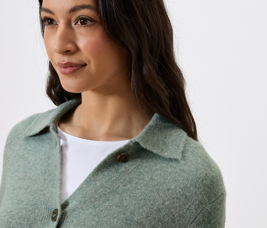 Portrét ženy s tmavými vlasmi v zelenom svetri s golierom a gombíkmi.