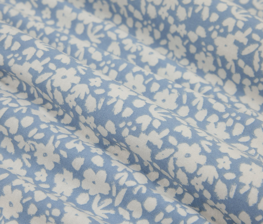 Detailný záber na modrú látku s malými bielymi kvetmi, vytvárajúci jemný a svieži vzor.