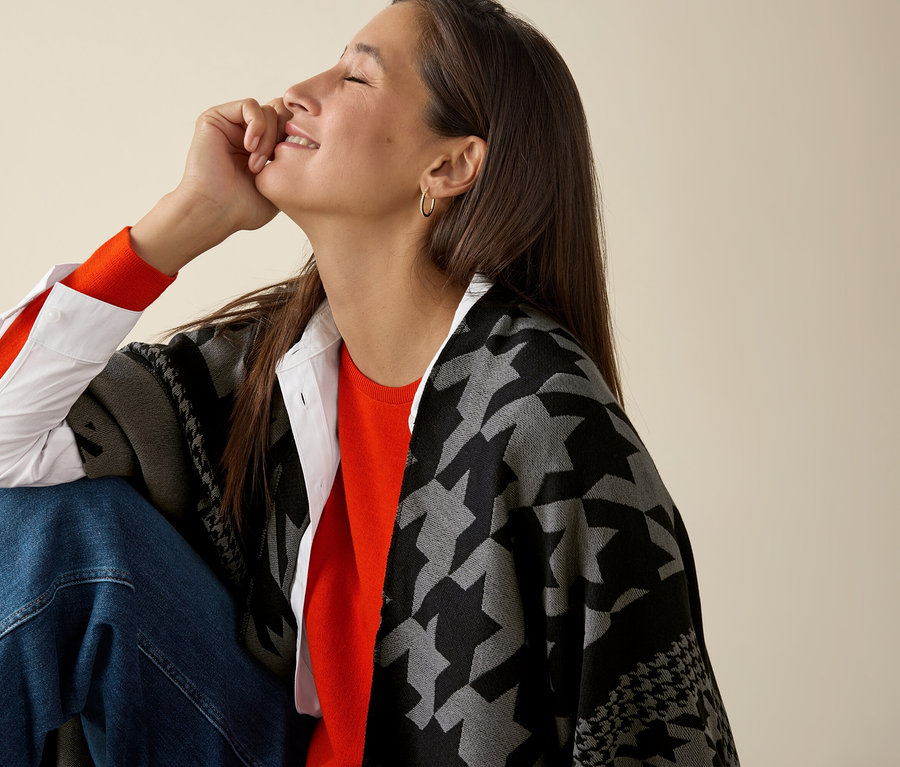 Žena sedí a má na sebe oranžový Mernio-Feinstrickpullover.