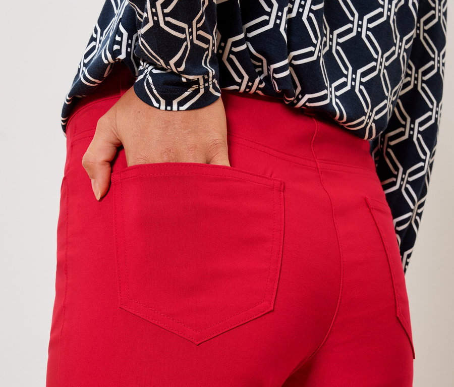 Žena vkladá ruku do zadného vrecka červených nohavíc.