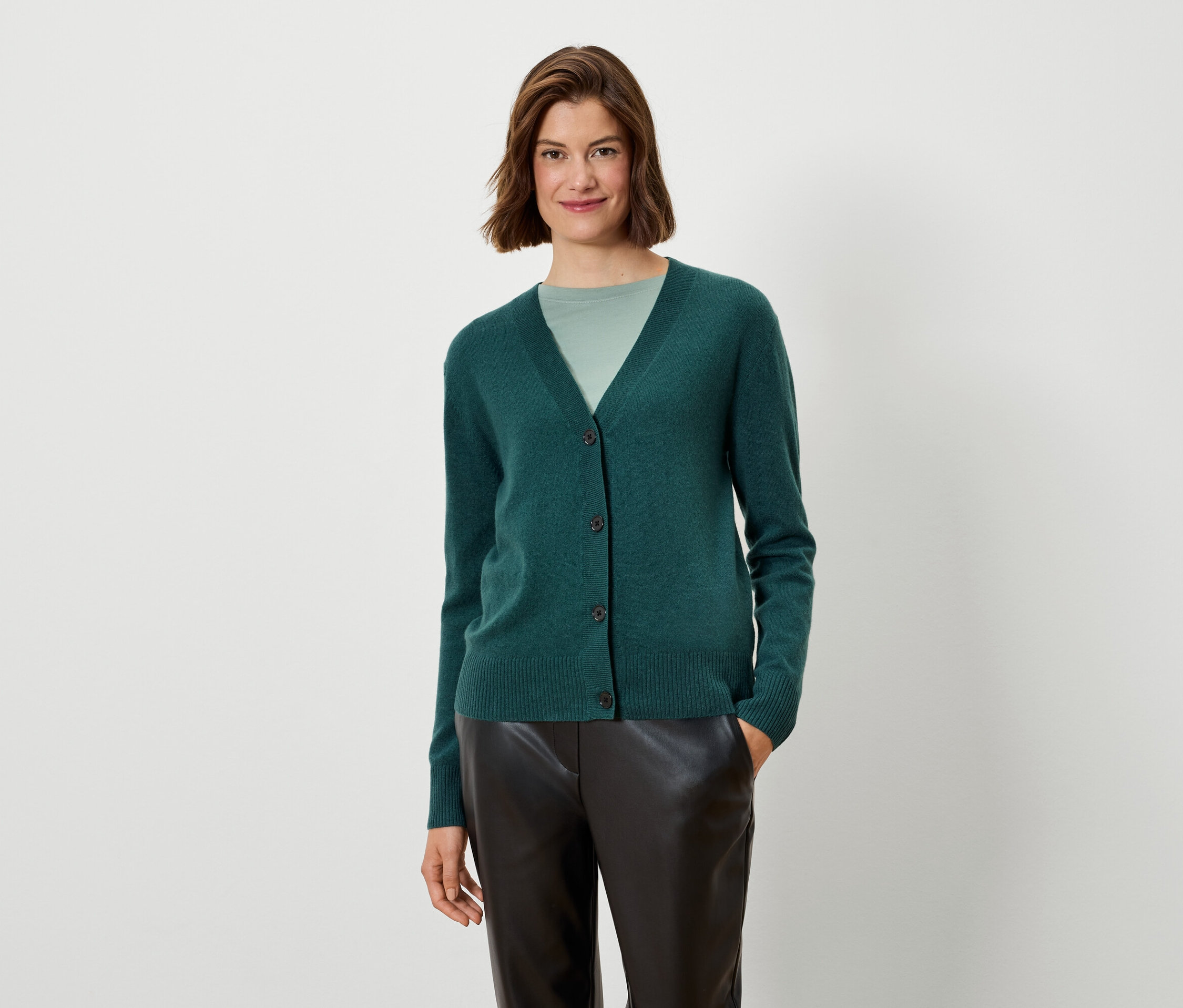 Žena má na sebe zelený kardigán a čierne nohavice.