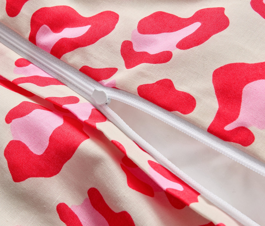 Detailný záber čiastočne otvoreného zipsu na látke s ružovými a červenými škvrnami.