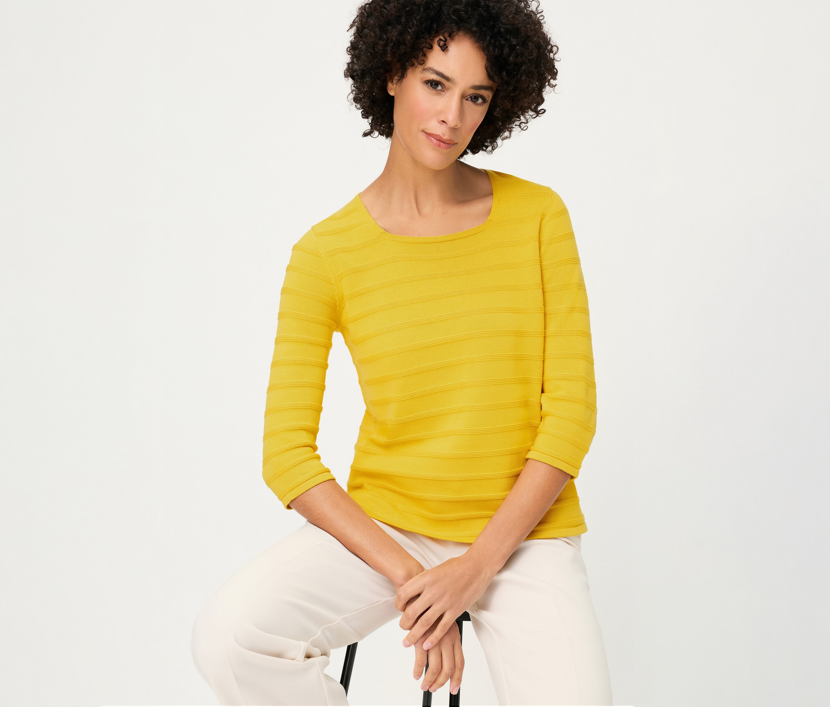 Žena sedí a má na sebe štruktúrovaný pulóver Olsen s 3/4 rukávmi žltej farby a svetlé nohavice.
