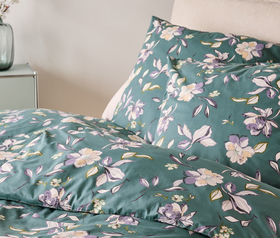 Detailný záber posteľnej bielizne s kvetinovým vzorom v zelenej, fialovej a bielej farbe.