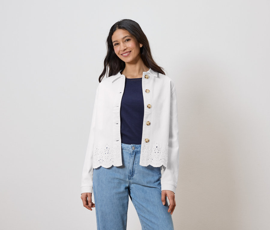 Žena má na sebe bielu bundu s dierkovanou potlačou cez tmavomodrý top a svetlomodré džínsy.