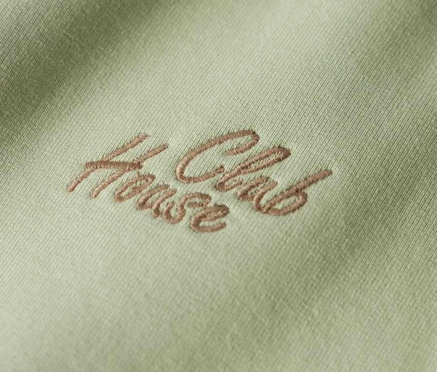 Detailný záber svetlozelenej látky s hnedou výšivkou "House Club".