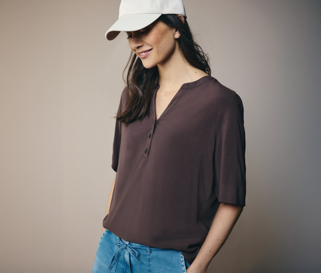 Žena v bielej čiapke a hnedej tunikovej blúzke CECIL.