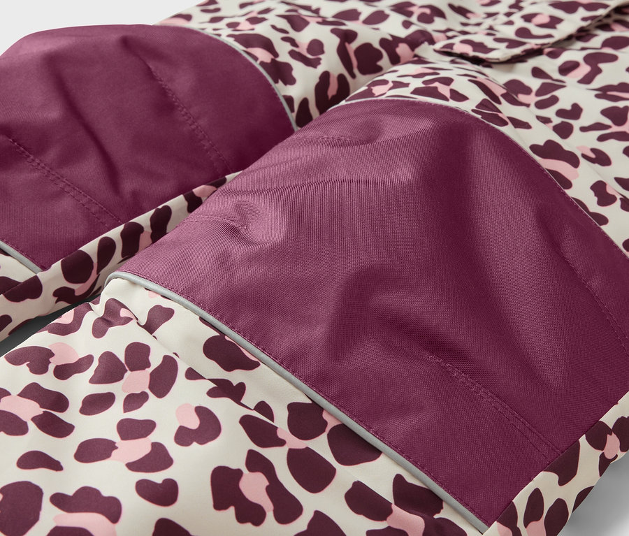 Detail oblečenia s leopardím vzorom v béžovej, tmavofialovej a ružovej farbe. Má tmavofialové nášivky na kolenách/lakťoch s reflexnými pásikmi.