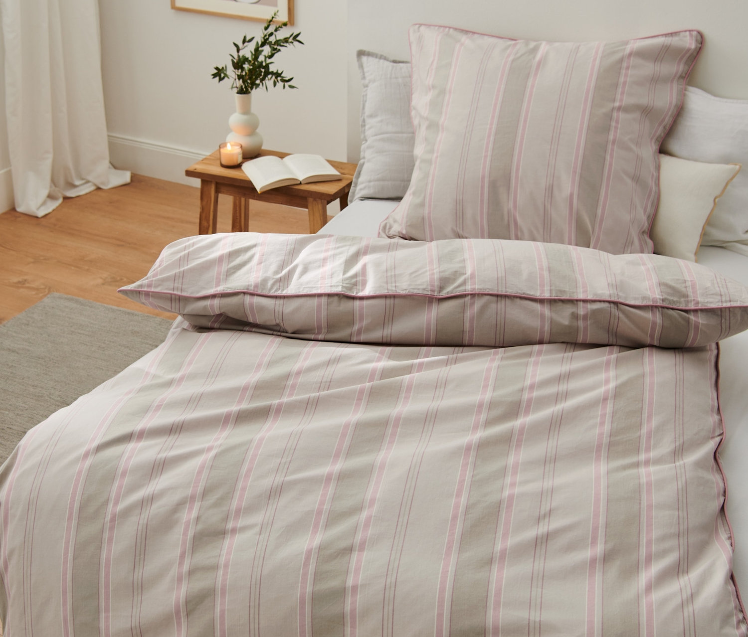 Spálňa s posteľou s prémiovou bavlnenou posteľnou bielizňou štandardnej a nadmernej veľkosti. Váza a kniha na nočnom stolíku.