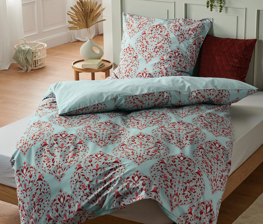 Posteľ s modrým obliečkom s červeným kvetinovým vzorom. Na posteli ležia tri Prémiové bavlnené posteľné bielizne štandardnej veľkosti.