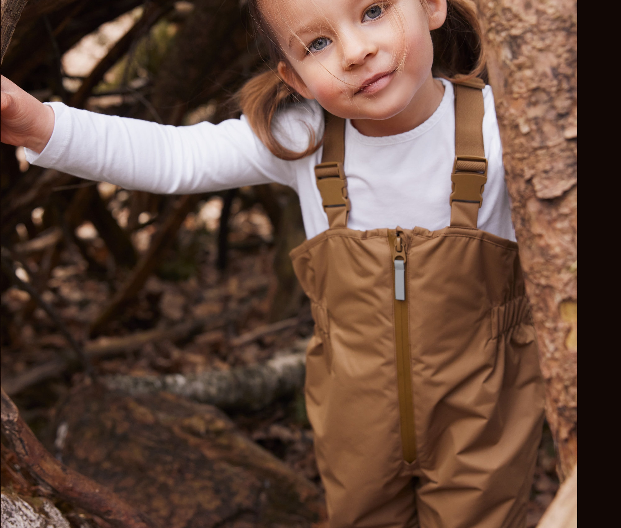 Dievča v hnedých nohaviciach do dažďa stojí pri strome.