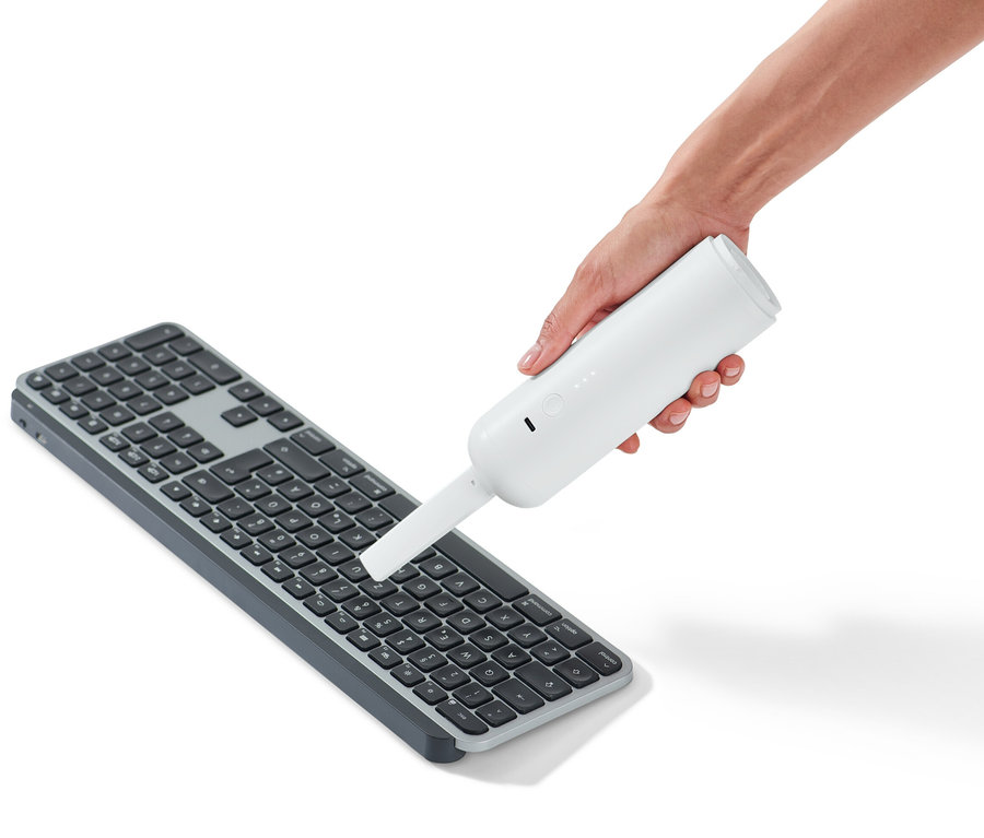 Ruka drží akumulátorový ručný vysávač nad klávesnicou.