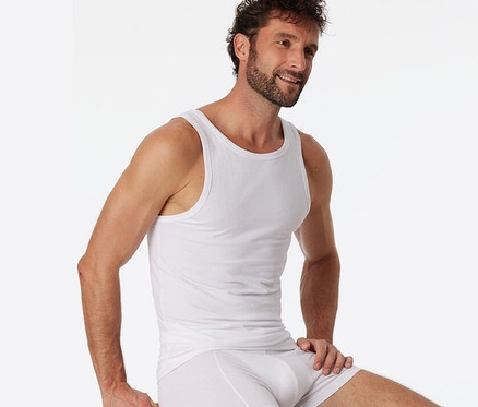 Muž sedí na stoličke a má na sebe biele tielko SCHIESSER s biobavlnou, 2 ks.