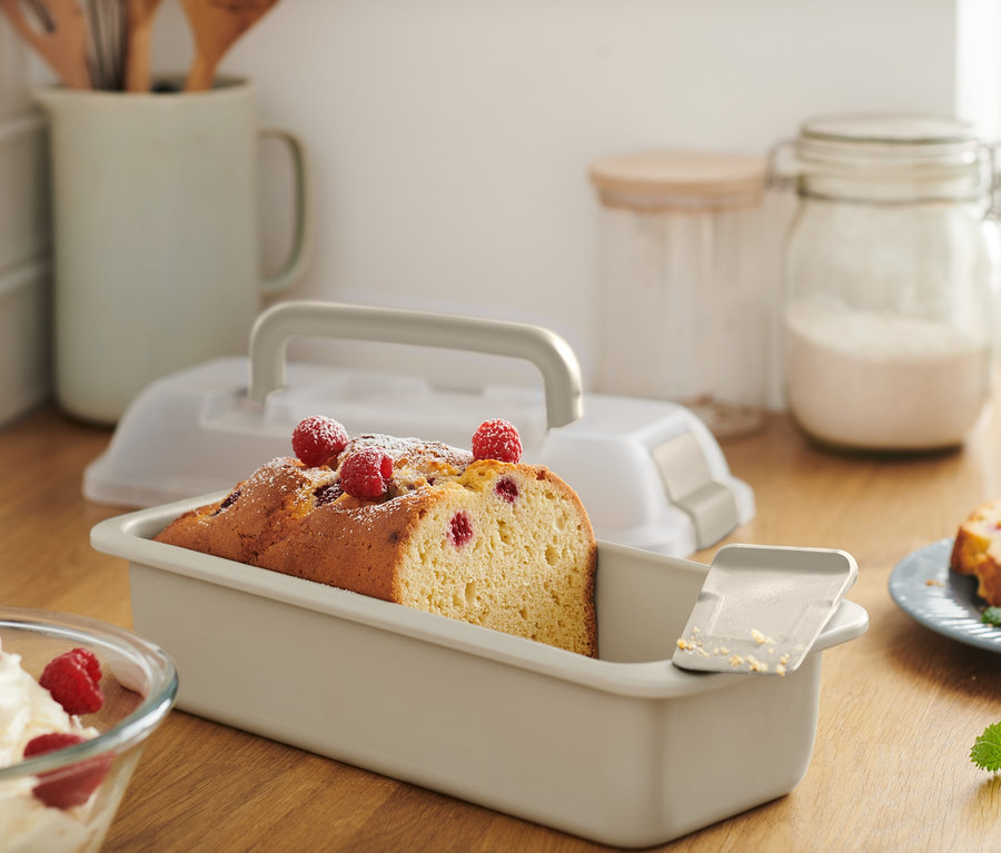 Nakrájaný koláč v hranatej forme na pečenie s vekom, posypaný práškovým cukrom a malinami.