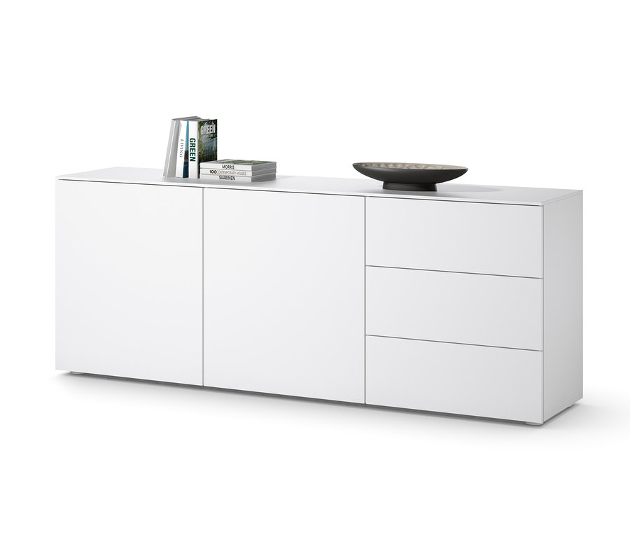 Biela odkladacia skrinka s tromi zásuvkami a dvierkami, na ktorej ležia knihy a miska.