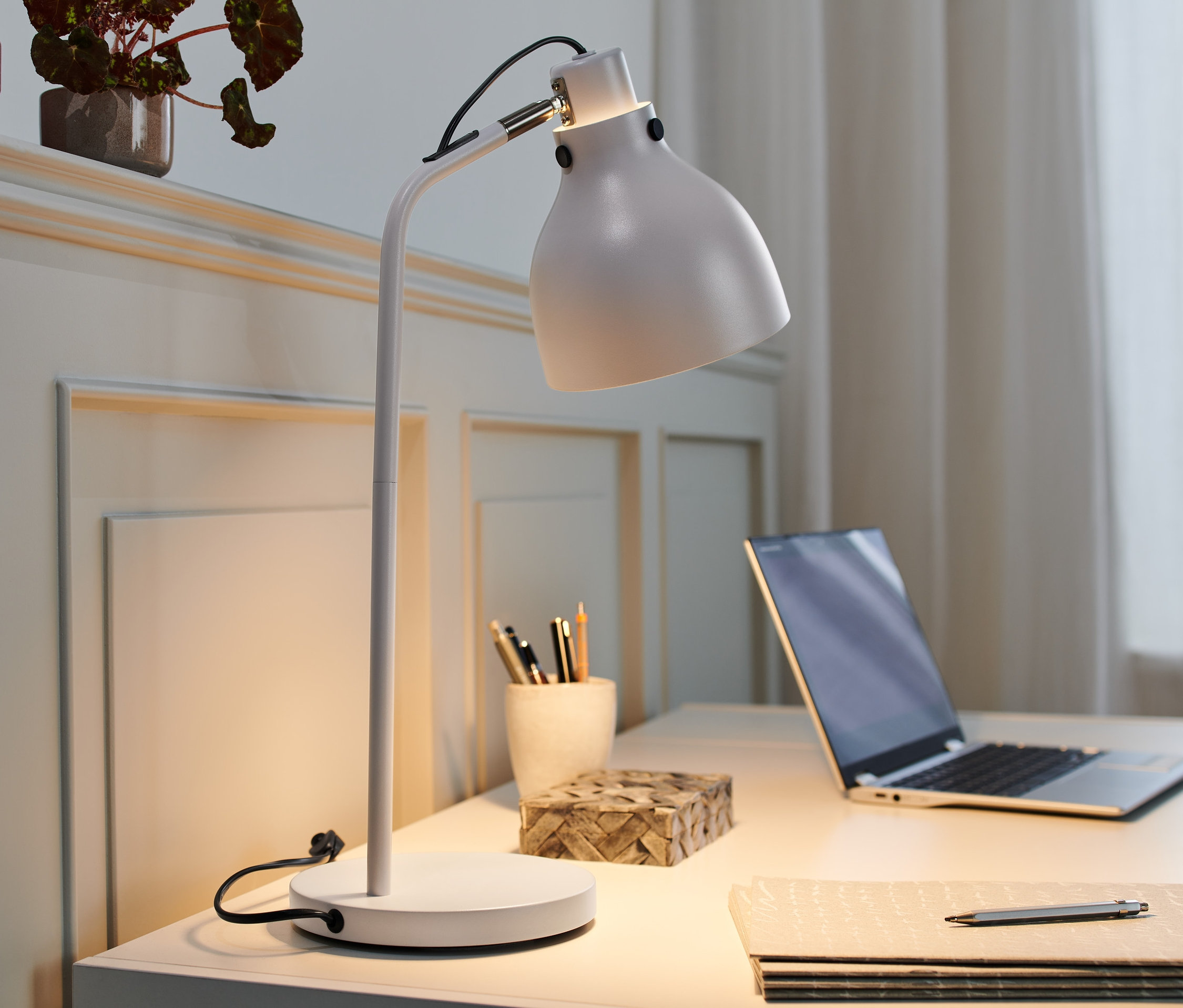 Stolová lampa z kovu na stole, vedľa notebooku a písacích potrieb.