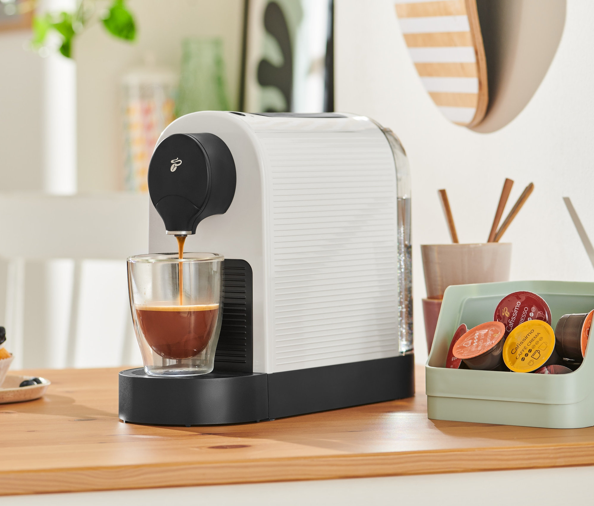 Kávovar Cafissimo pure+, biela, plní kávu do sklenice. V pozadí je cupcake.