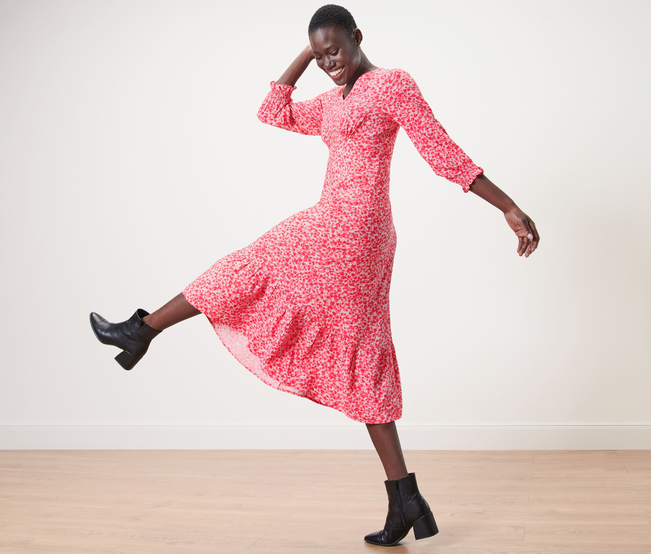 Žena v maxišatách s potlačou a čiernych členkových topánkach pózuje na drevenej podlahe.