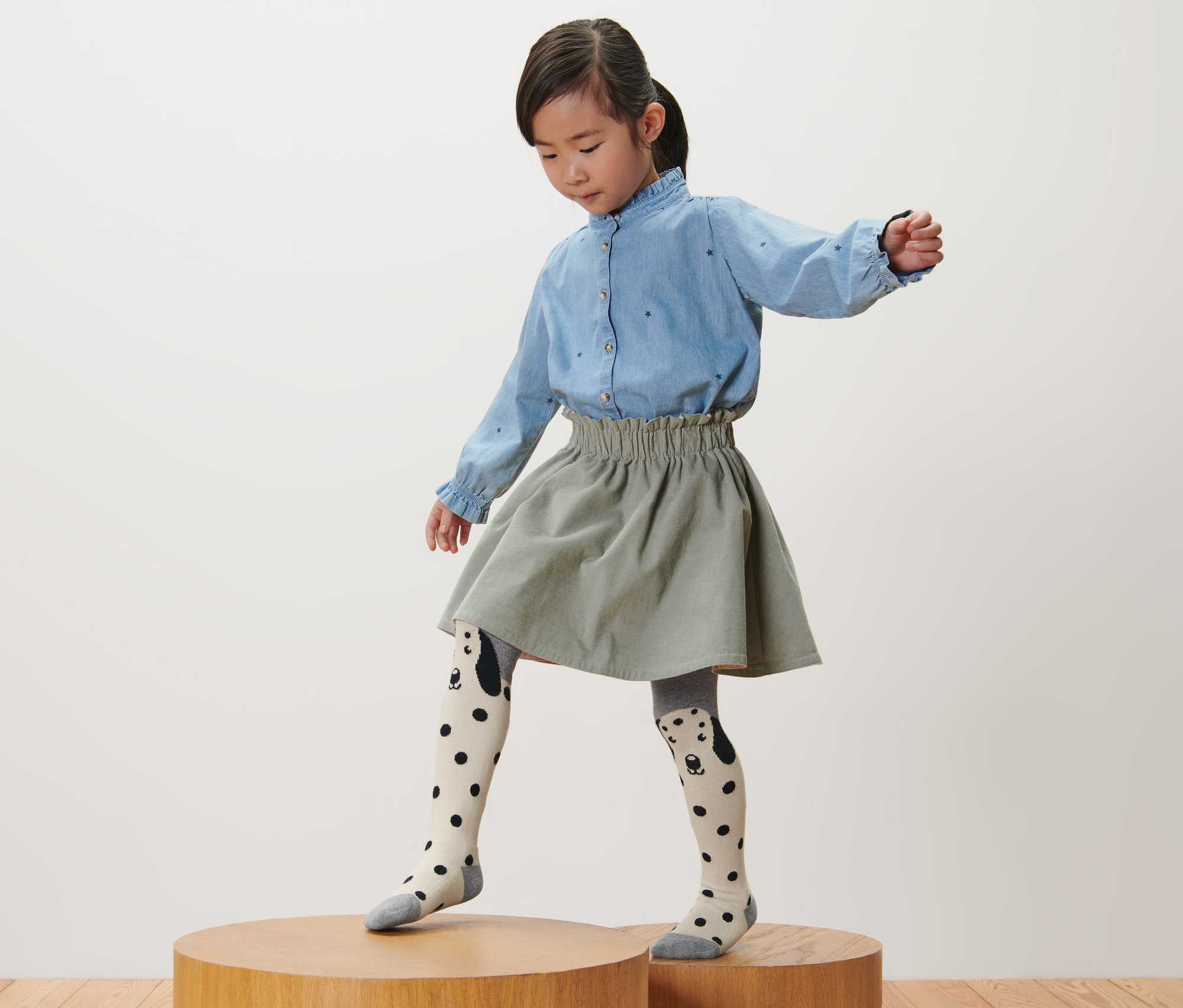 Dievča stojí na drevenom podstavci a má na sebe ružové, sivé a vínové detské pančuchy, 3 ks.