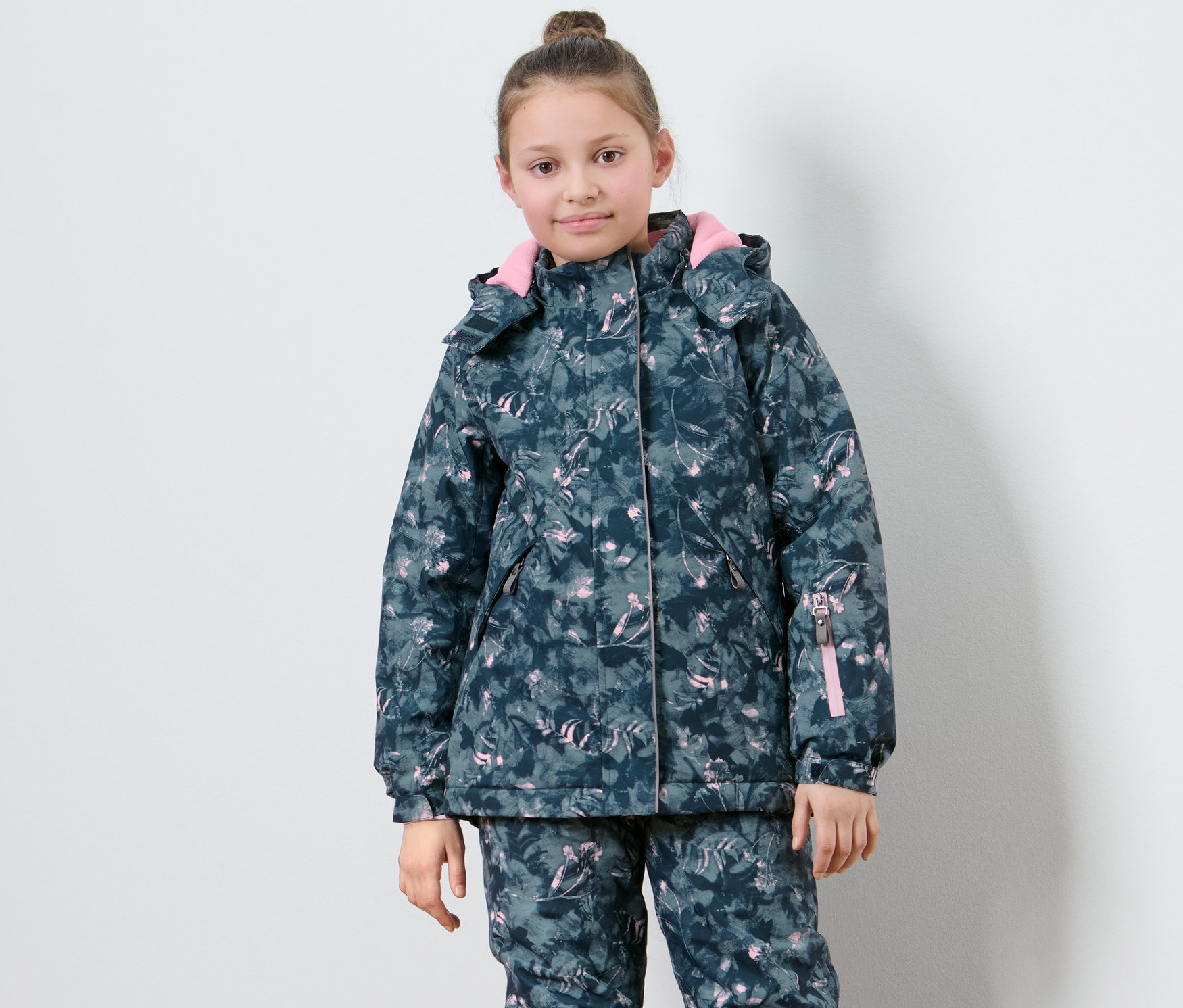 Dievča pózuje v detskej lyžiarskej bunde s potlačou.